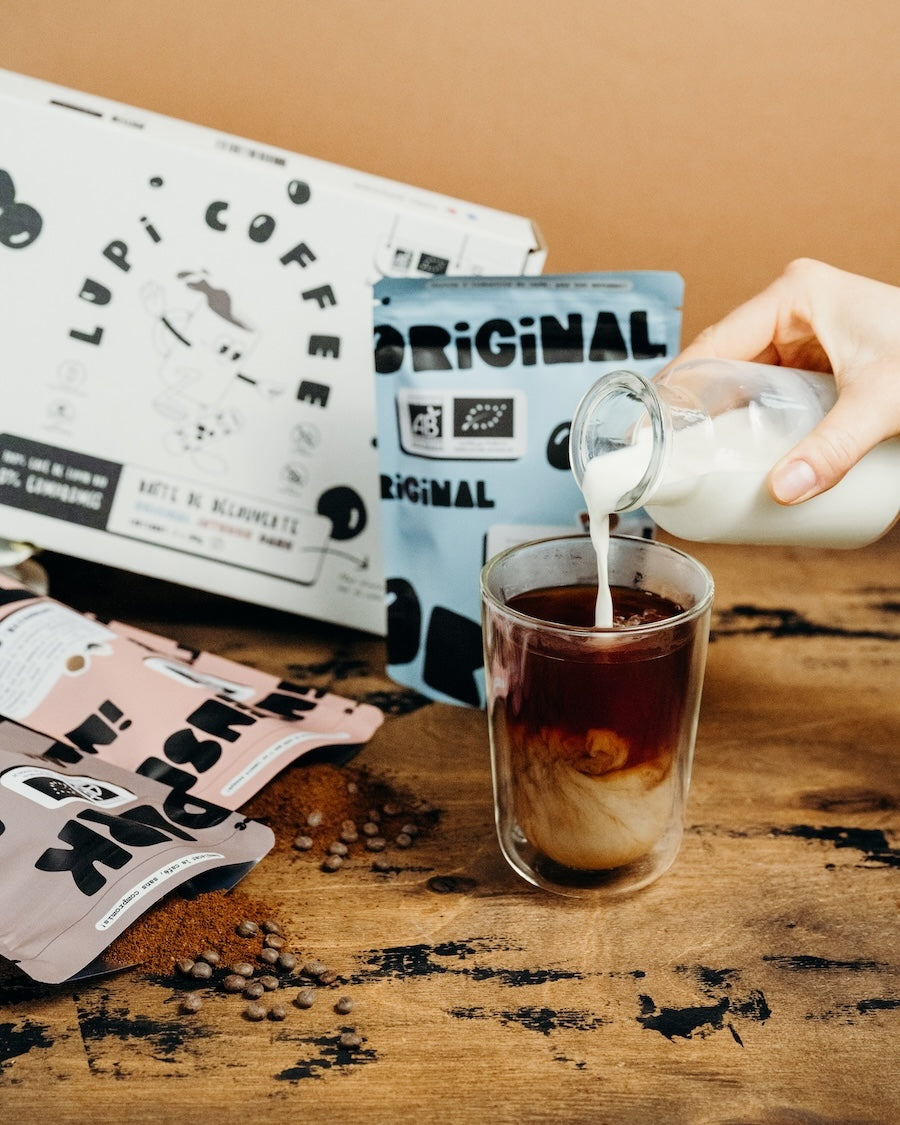 Un café de lupin froid avec du lait sur une table en bois, à côté de la boîte de découverte Lupi Coffee